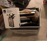 Photo of a box filled with various metal frames and the Umbra Optic display vessel box on top.