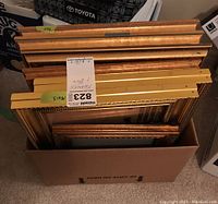 Photo showing multiple gold-toned picture frames stacked inside a box, various sizes, some ornate with carved detail.