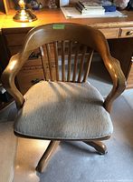 Front view of the wood swivel office chair with beige seat cushion, showing curved armrests and vertical slatted backrest.