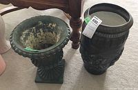 Side view of two ceramic planters: green pedestal planter with fluted design and a dark vase-shaped planter