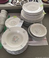 Stack of various sized plates and bowls in white with floral Valencia pattern arranged on table, showing quantity and stacked arrangement.