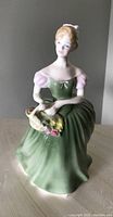 Full front view of the Royal Doulton Claressa figurine showing seated female figure in green and pink dress holding a basket of flowers