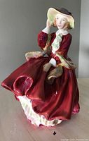 Front angle view of Royal Doulton porcelain figurine in red dress and hat, titled 'Top of the Hill'.