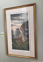Photo showing the full front view of the framed print with the art depicting a woman and child by the sea at sunset, gold ornate frame.