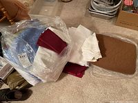 Collection of various folded table linens including padded placemats and napkins inside a clear plastic bag and on floor.