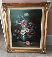 Full view of framed floral artwork showing gold decorative frame and floral bouquet in blue vase on a dark background.