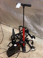 Photo showing Blackburn Air Tower 3 floor pump standing vertically, red body, pressure gauge near base, black handle and footrest, also showing part of black HDX portable compressor and bicycle rack near.