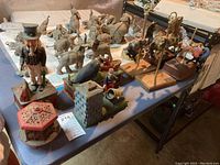 Photo showing a table with four cast iron banks, two carousel horse figurines and two carousel horse music boxes with loose horses on stands.