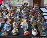 Overview of multiple figurines and candle toppers on a black table surface with natural light