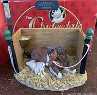 Front view of Clydesdale mare lying with foal inside stall, with original box in background