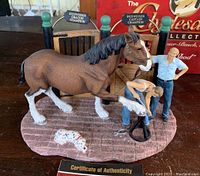 Figurine titled Getting Shod showing a Clydesdale horse on a textured surface with two handlers attending, accompanied by a small dog figure. Display includes certificate of authenticity.