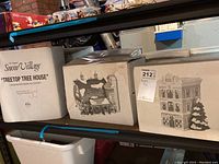 Boxes of Department 56 Snow Village collectibles showing various buildings from the set including Treetop Tree House and Village Market.