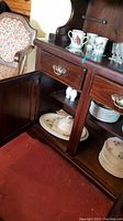 Partial view inside wooden cabinet showing Butterfly Meadow partial dinnerware set including plates and bowls, and some serving platters on bottom shelf.