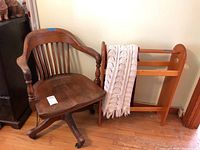 Wooden office chair next to wooden blanket rack with knitted blanket on hardwood floor.