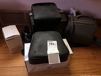 Overview of lot items on floor including black leather Bell & Howell projector case, binoculars, Polaroid camera box, scanner and carrying case.
