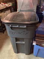 Front view of gray Rubbermaid garbage pail with marked exterior and attached lid.