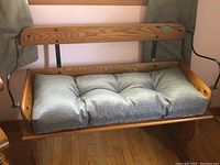 Front view of the bench with the grey tufted seat cushion on the wooden seat base, showing curved wooden arms with black metal supports and wide backrest with screws visible.