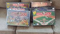 Lot of six Monopoly board games arranged on carpeted floor, showing various themed editions with colorful art on boxes.