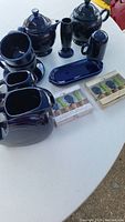 Overview of cobalt blue Fiesta ceramic pieces with two sets of packaged cheese spreaders on a white table.