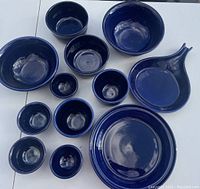 Photo showing 13 cobalt blue Fiesta ware pieces including various sized bowls, a plate, a cup, and fish-shaped dish