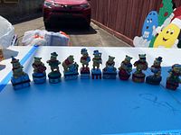 All 11 Disney Winnie the Pooh trinket boxes spaced in a line on a blue table outdoors under sunlight
