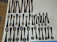 Display of black-handled knives, forks, and spoons laid out in rows on a counter.