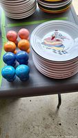 Photo showing 4 pairs of Fiesta salt and pepper shakers in orange, red, blue, turquoise shades next to stacked Fiesta plates.