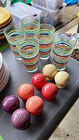 Photo showing four pairs of Fiesta Ware salt and pepper shakers in purple, orange, red, and cream, alongside five colorful banded glasses.