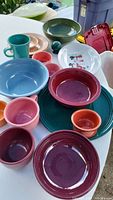 Overall view of assorted Fiesta Ware dinnerware in various colors including blue, maroon, pink, green, and white snowman dish with salt shaker