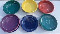 Top-down view showing seven Fiesta Ware bowls in multiple colors arranged in a circle on a white table.