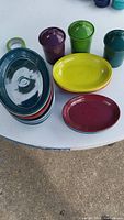 Top view of Fiesta Ware ceramic lidded canisters with an assortment of six oval platters in various colors displayed on a white surface outdoors.