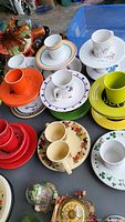 Top view showing multiple Fiesta mugs and colorful matching plates in red, orange, yellow, green, and white volcanic glaze ceramic.