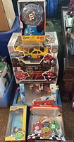 Stack of several M&M collectible candy dispensers in boxes including spin dispenser, firetruck, car, barnstorming, Rockin Roll dispenser plus an LED desk lamp shown in original packaging on floor.