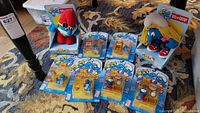 Wide view of lot showing four packaged Smurf poseable figures laid out and two large stuffed Smurf plush toys standing in boxes.