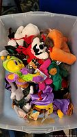 Multiple Warner Bros plush bean bag toys inside a clear Rubbermaid tote, posing details of characters like Tweety Bird and Taz showing facial expressions, colors, and tags.