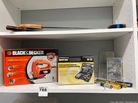 Shelf with boxed Black & Decker jigsaw, Hurricane spark plug maintenance kit, small screwdriver set, and clear container with fittings inside.