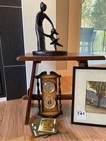 Photo showing black metal sculpture on wooden stool, vintage barometer below stool, framed Lake Geneva print leaning on stool, and coasters on floor