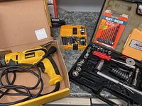 Wide image showing DeWalt drill in a box, yellow case with drill bits, Black & Decker 10 drill bit set packet, and black case with sockets and ratchet