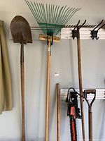Full view of multiple garden tools including shovel, rake, hoe, Remington electric hedger, and additional tools, showing condition and overall lot contents.