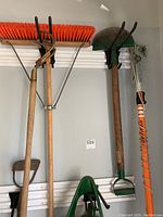 Full view of lot hanging on wall showing broom, shovel, edger, spreader, and tree branch trimmer