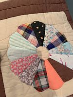 Close-up photo of a single circle quilt block showing various patterned fabric segments handstitched together on a beige background with brown border.