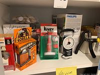 Shelf with Gorilla glue, Krazy glue, hand exerciser tools, and boxes of Philips light bulbs