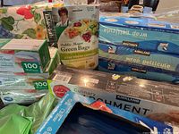 Photo of unopened Kirkland kitchen wrap products, Debbie Meyer Green Bags, vinyl tablecloth, and multiple Ziploc boxes arranged on a table.