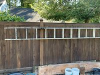 Photo of extended aluminum ladder hung horizontally on a wooden fence showing overall length and condition.