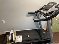 Full view of treadmill on mat with accessory kit box and folded light green covers on deck