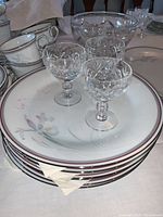 Stack of dinner plates with floral pattern and 5 cut crystal aperitif glasses on top.