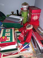 Overview photo showing stacked boxes of Christmas cards, holiday tins, fabric gift bags, and a snowman decorative container