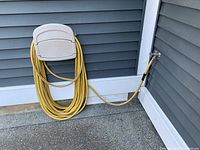 Yellow Riviera garden hose coiled and attached to a wall faucet, showing length and condition.