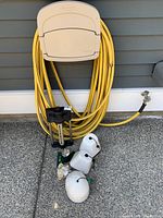 Yellow outdoor hose coiled on faucet with hose attachments and faucet covers on ground