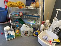 Wide view showing wire rack with cleaning cloths and pads, plastic pail with sprayers, cleaning chemicals, brushes, and rope on top shelf.